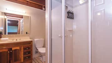 A bathroom with a wooden vanity, a toilet, a shower with glass doors, and a tiled floor.