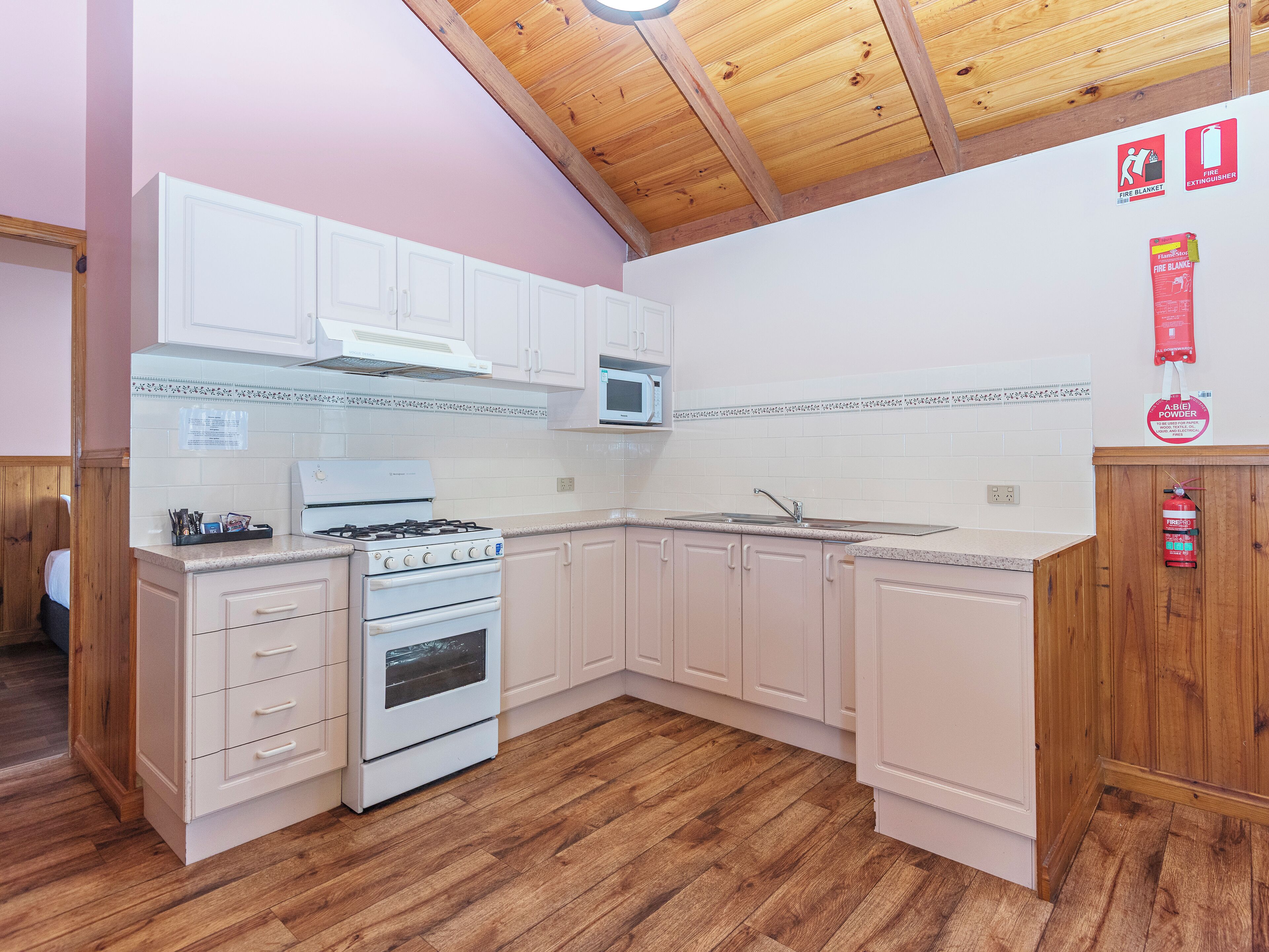 Una cocina con armarios blancos, estufa, microondas y suelo de madera.