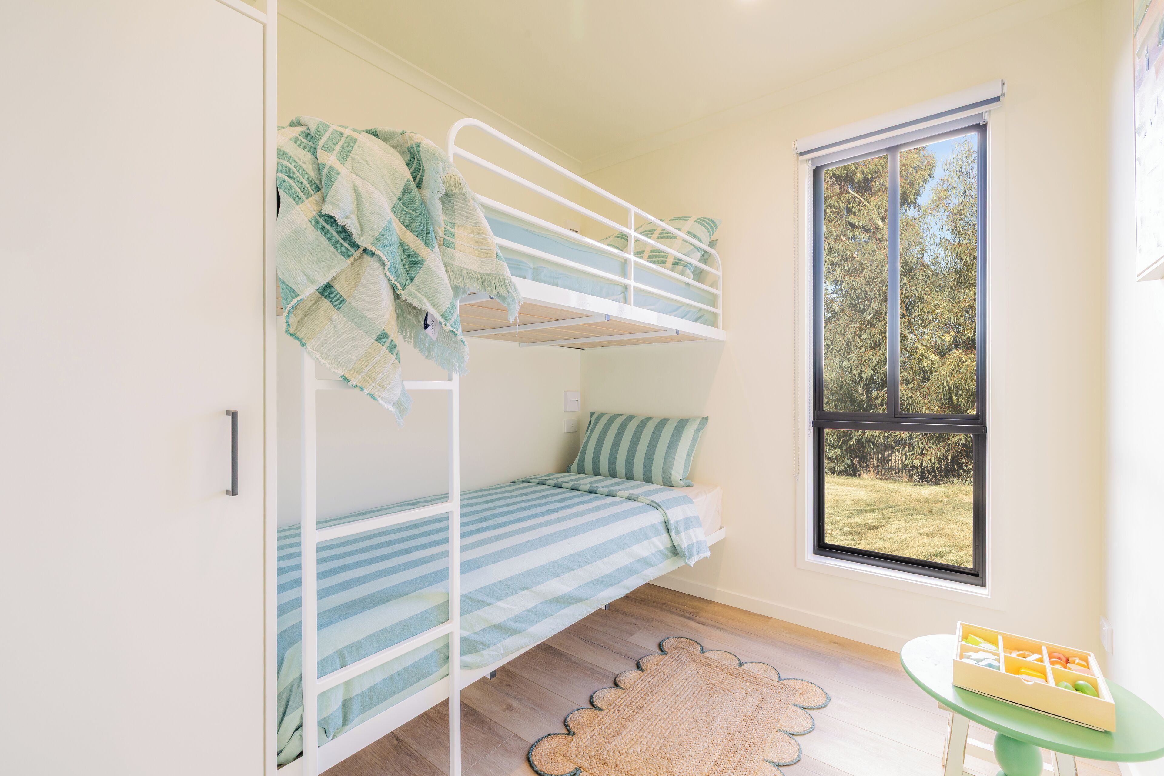 A bunk bed room with a window, a small table with a box, and a door.