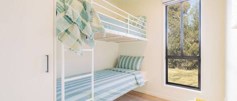 A bunk bed room with a window, a small table with a box, and a door.