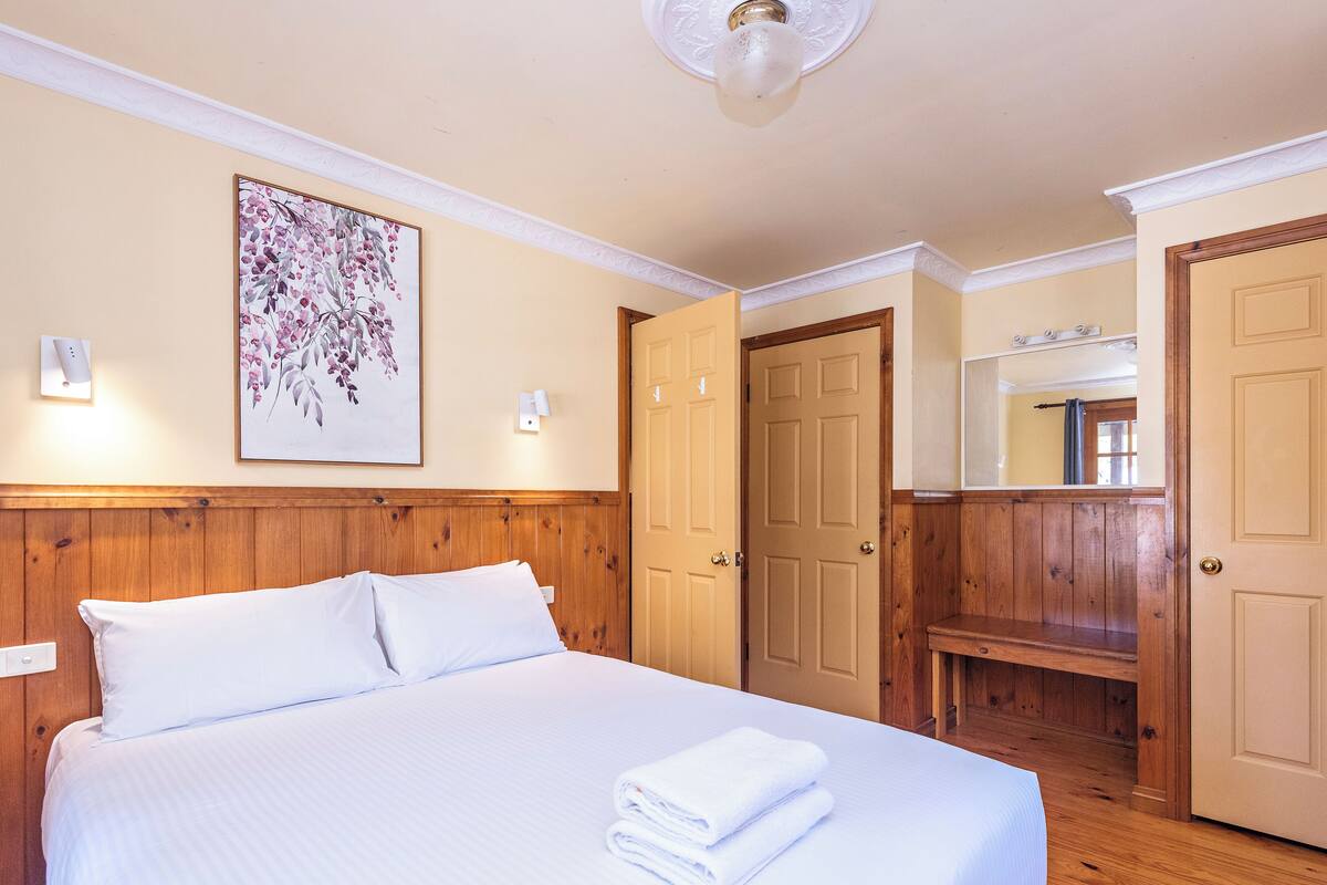 A hotel room with a bed, a wall-mounted light, a door, and a mirror.
