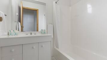 Un baño moderno con tocador blanco, un espejo grande y zona de ducha.
