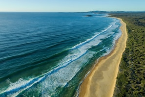 Luchtbeeld van een strand met helderblauw water, een zandstrand en weelderige begroeiing.