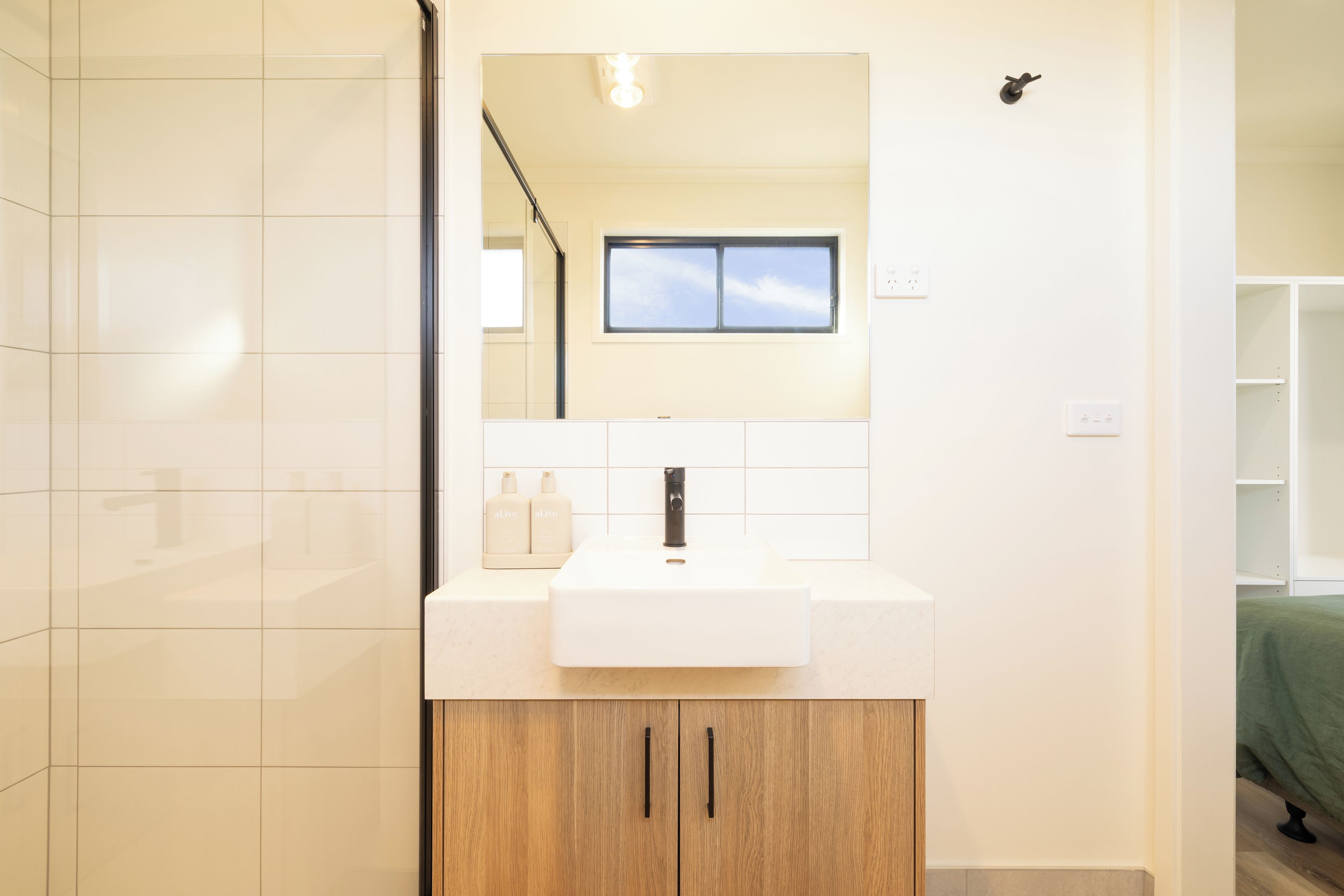 Een moderne badkamer met een wit wastafel, een houten kastje en een spiegel erboven.