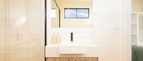 Een moderne badkamer met een wit wastafel, een houten kastje en een spiegel erboven.