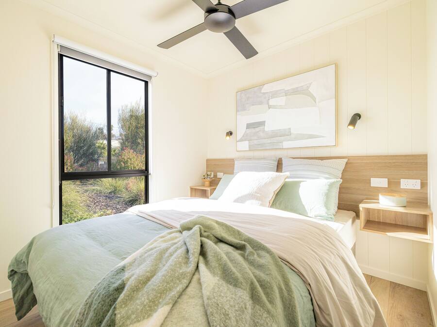 A bedroom with a bed, a ceiling fan, a window, and a wall-mounted light fixture.