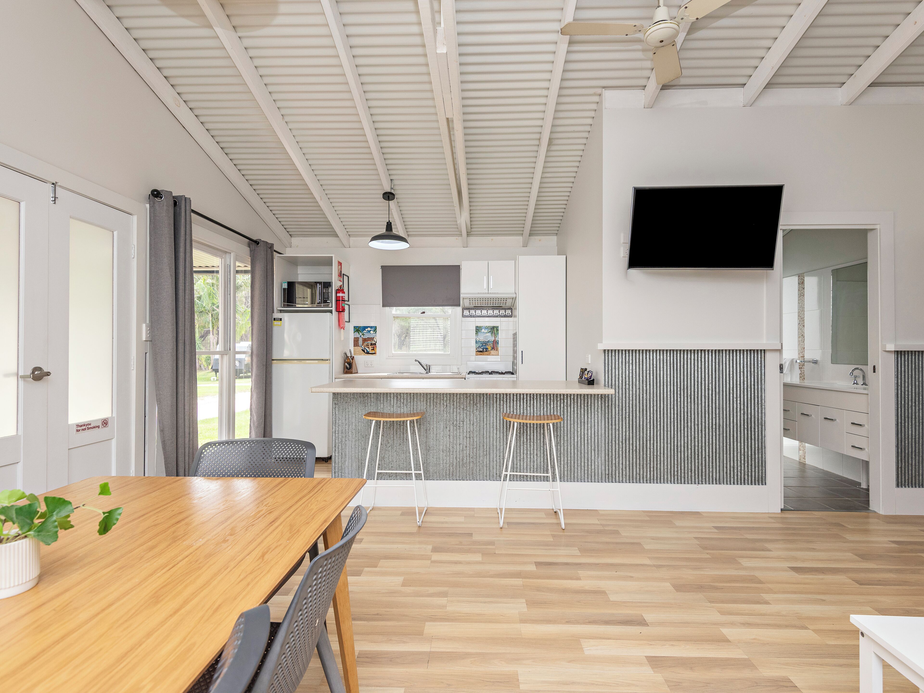 Una cocina moderna con una isla central, un comedor con mesa y sillas de madera, y un televisor montado en la pared.