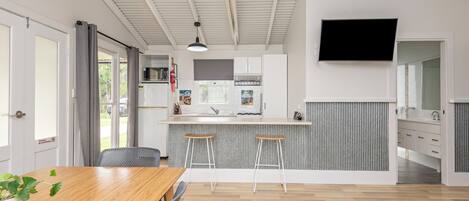 Una cocina moderna con una isla central, un comedor con mesa y sillas de madera, y un televisor montado en la pared.