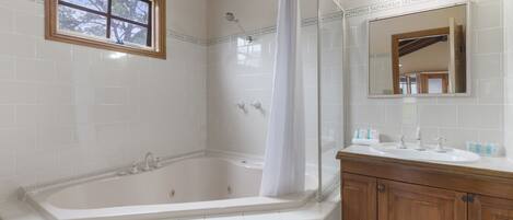 A bathroom with a bathtub, a shower, a vanity with a mirror, and a window.
