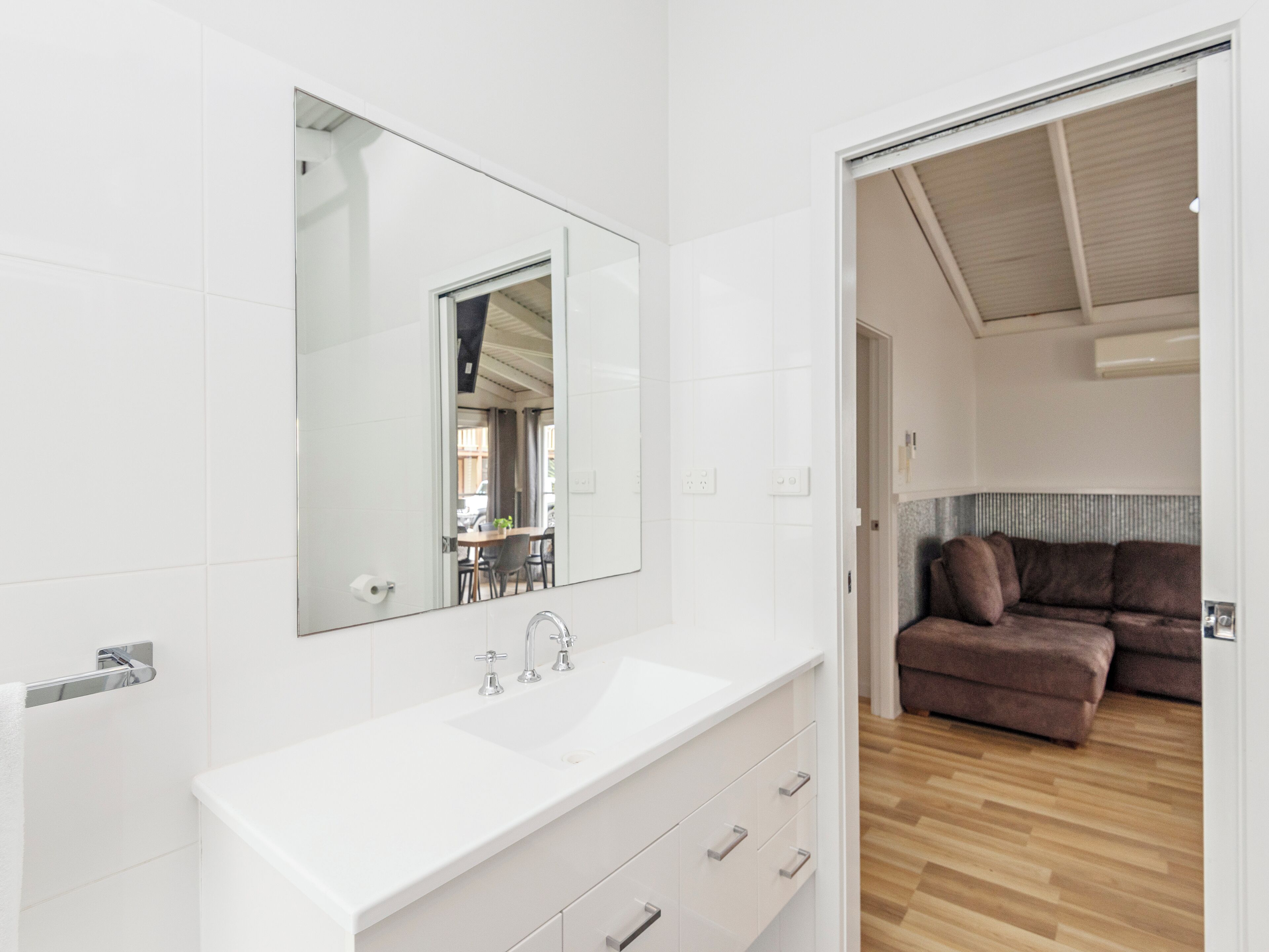 A modern bathroom with a white sink, a large mirror, and a wooden floor.