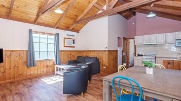 A cozy cabin interior with wooden walls, a dining area, a kitchen, and a living room with a couch and chairs.