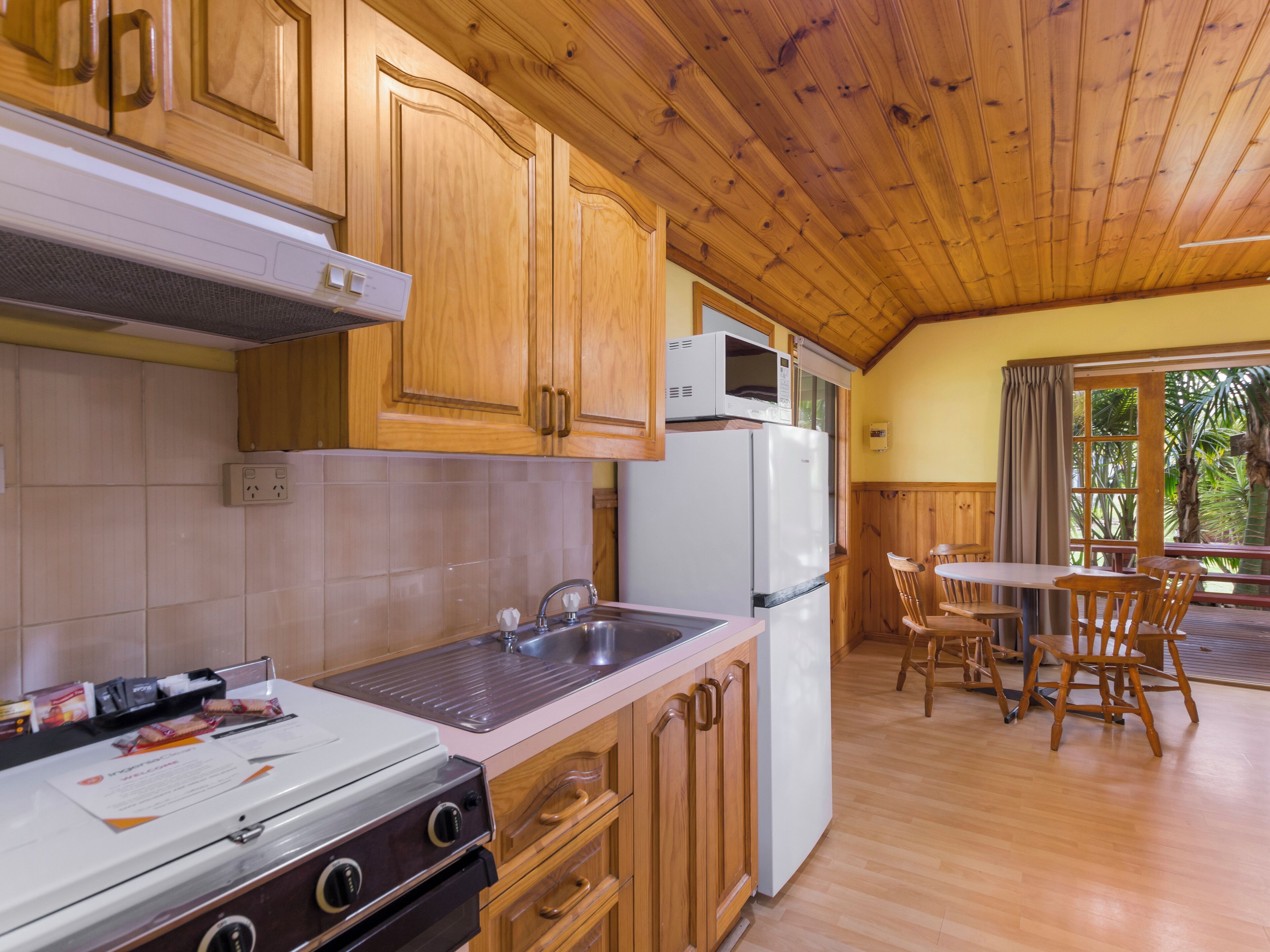 A kitchen with wooden cabinets, a microwave, a refrigerator, a sink, and a dining area with chairs.