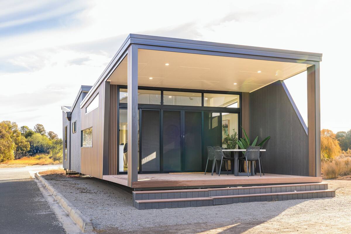 A modern house with a large glass door, a wooden deck, and a table with chairs outside.