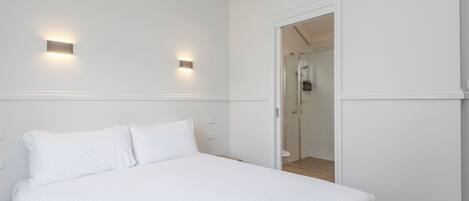 A hotel room with a bed, two wall-mounted lights, and a glass-enclosed shower.