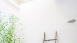 Un petit patio clos, agrémenté d’une plante en bambou, d’un tabouret vert et d’une échelle en bois adossée à un mur blanc.