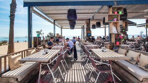 En udendørs restaurant med træborde og bænke med udsigt over en strand.