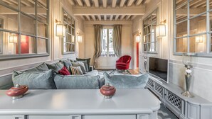 A spacious living room with a large sectional sofa, a red armchair, and a television. The room has large windows with curtains and wall-mounted lamps. - Ca' Dell'Opera Terrace (Venice)