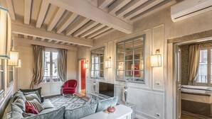 A spacious living room with a sofa, a coffee table, and a red armchair. There is a television on a stand, and the room has large windows with curtains. - Ca' Dell'Opera Terrace (Venice)