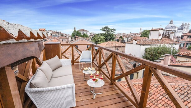 A wooden deck with a white wicker sofa and a small table with drinks and snacks. - Ca' Dell'Opera Terrace (Venice)