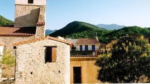 A stone building with a bell tower, surrounded by greenery and mountains. - Beautiful village home in the foothills of the Pyrenees (Finestret)