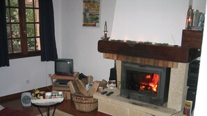 A cozy living room with a fireplace, a television on a wooden stand, and a small table with a cup. - Beautiful village home in the foothills of the Pyrenees (Finestret)