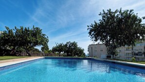 Ein klarer, blauer Swimmingpool, umgeben von Bäumen und einem mehrstöckigen Gebäude.