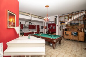 A billiards table with a pool cue, a dining table, and a bar area with stools.