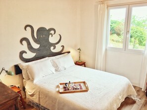 A bed with a decorative headboard, a bedside table with a lamp, and a window with a view of greenery.