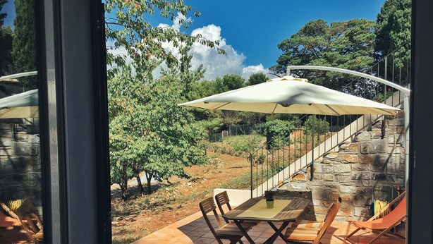 A patio with a table and chairs, a white umbrella, and a stone staircase. - Octo bookcase, sanctuary, organic, design, relaxation. (Imperia)