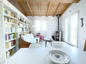 A cozy living room with a white sofa, a bookshelf, a fireplace, and a dining table. - Octo bookcase, sanctuary, organic, design, relaxation. (Imperia)
