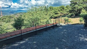 A gravel pathway leading to a red-tiled roof structure with a metal railing, surrounded by greenery and trees. - Octo bookcase, sanctuary, organic, design, relaxation. (Imperia)