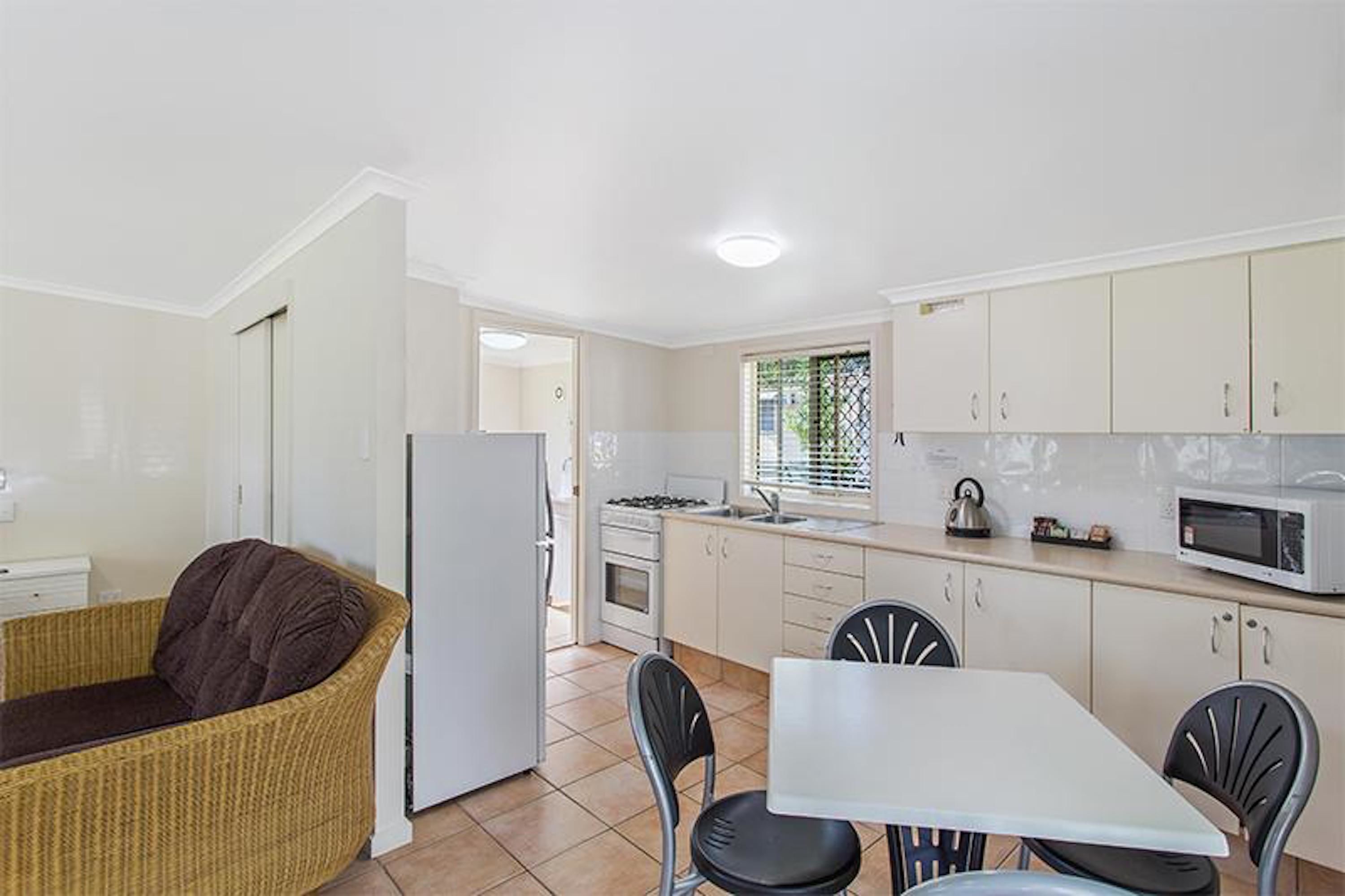 Una cocina compacta con armarios blancos, un refrigerador blanco, estufa a gas, microondas y un comedor con mesa blanca y sillas negras.