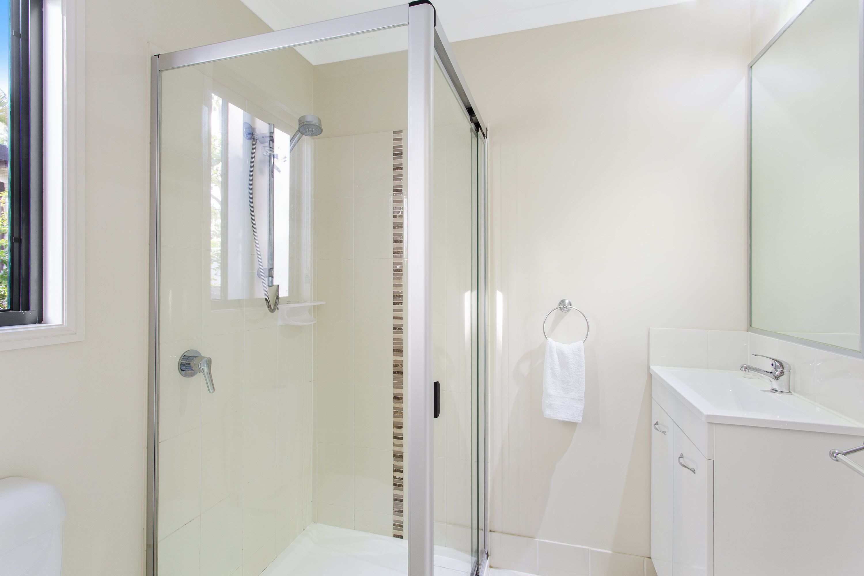 A modern bathroom with a glass-enclosed shower, a white sink, and a large mirror.