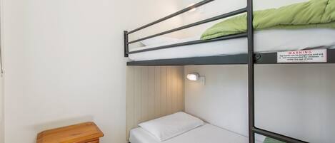 A bunk bed with a warning sign, a wooden nightstand, and a wall-mounted light fixture.