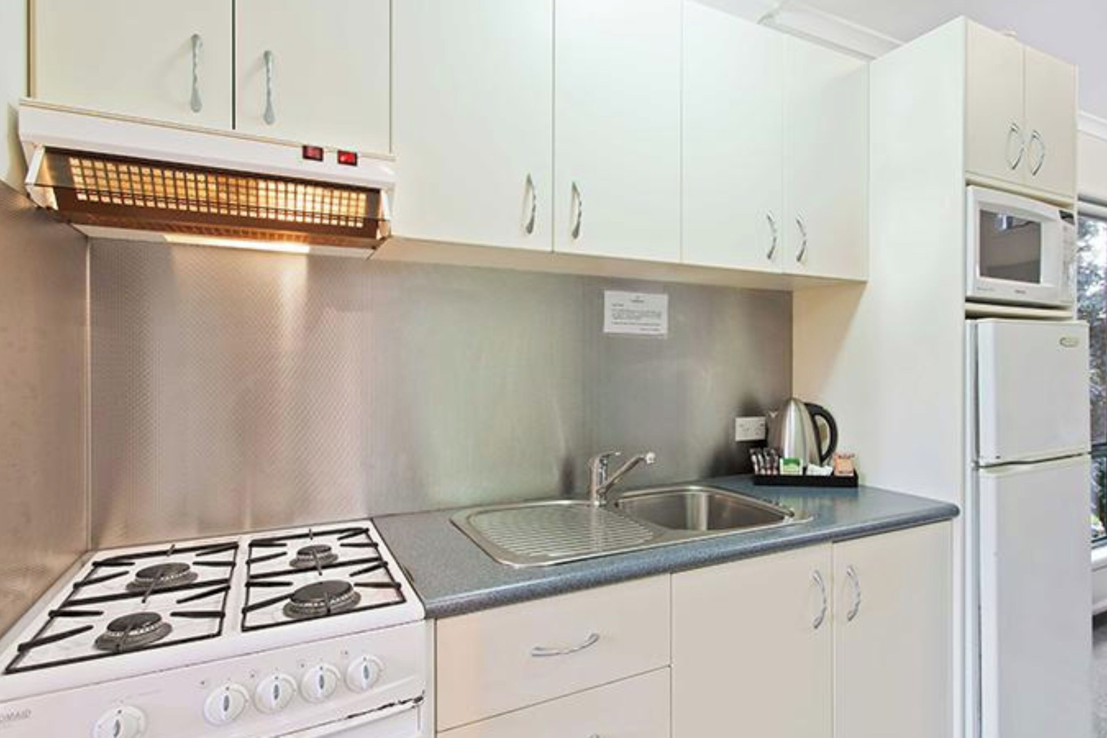 A kitchen with white cabinets, a gas stove, a sink, and a microwave.