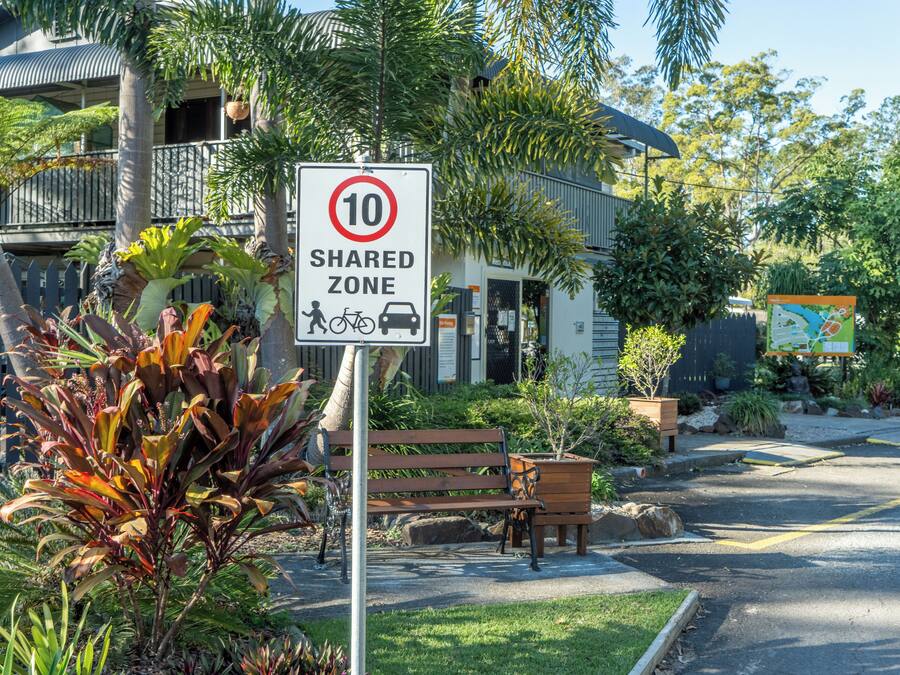 Señal de zona compartida con límite de velocidad 10, un banco y abundante vegetación.