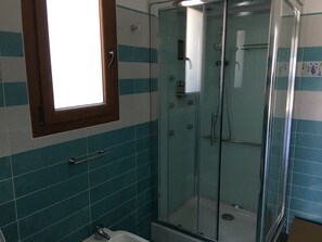 Ein Badezimmer mit Duschkabine aus Glas, einem Fenster über dem Waschbecken und blauen und weißen Fliesenwänden.
