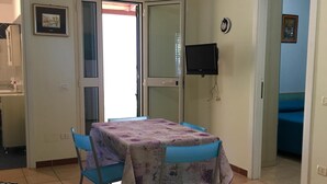 A dining area with a table and chairs, a television mounted on the wall, and a door leading to another room. - MIMOSA A Three-room detached house in the Villa Carla Residence for realiz (Vieste)