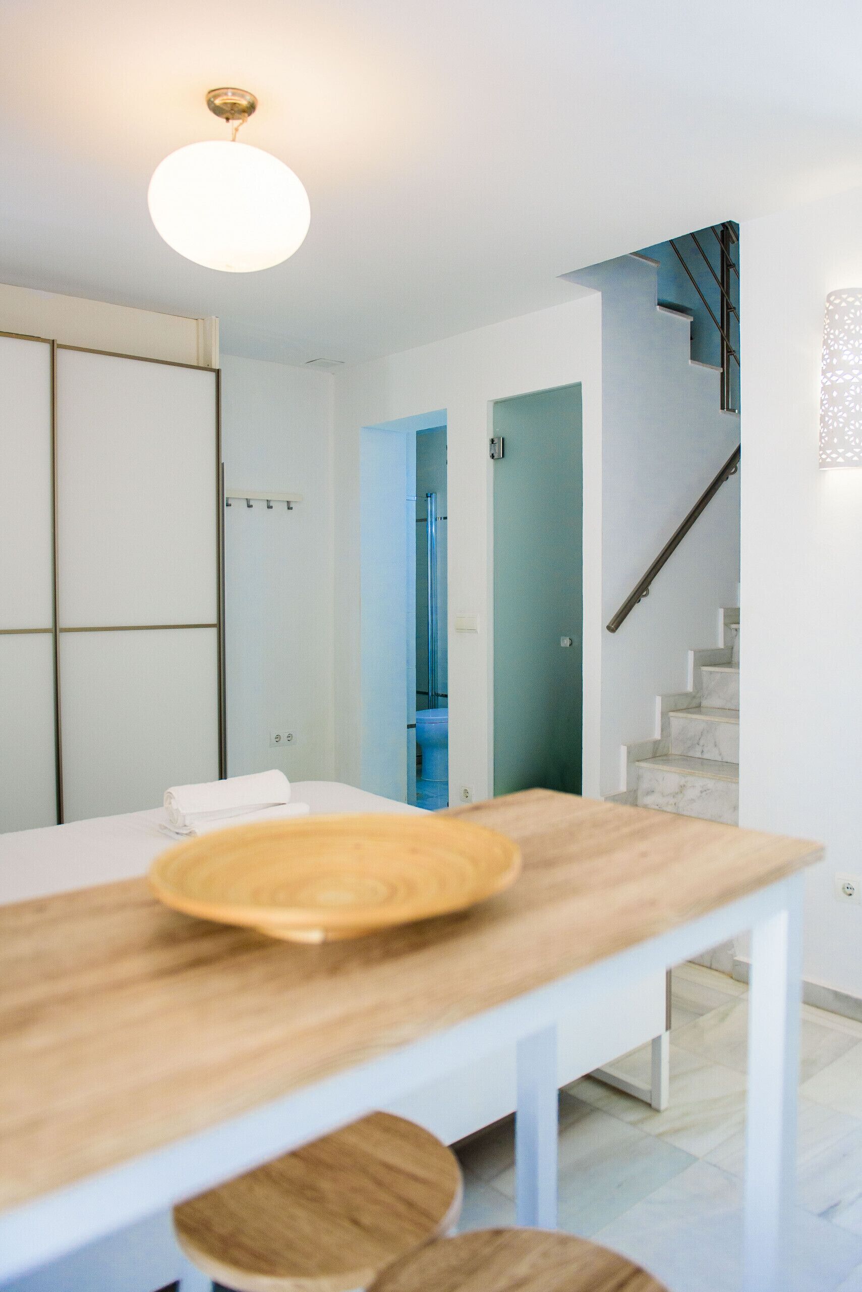 Una cocina moderna con una mesa de madera, una lámpara colgante y una escalera que lleva a una habitación azul.