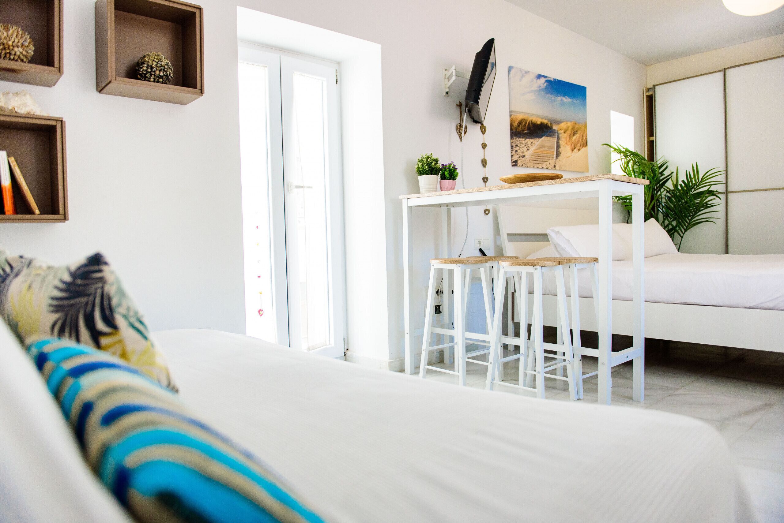 Un dormitorio moderno con una cama, un escritorio con dos sillas, una mesita y un estante de pared con objetos decorativos.