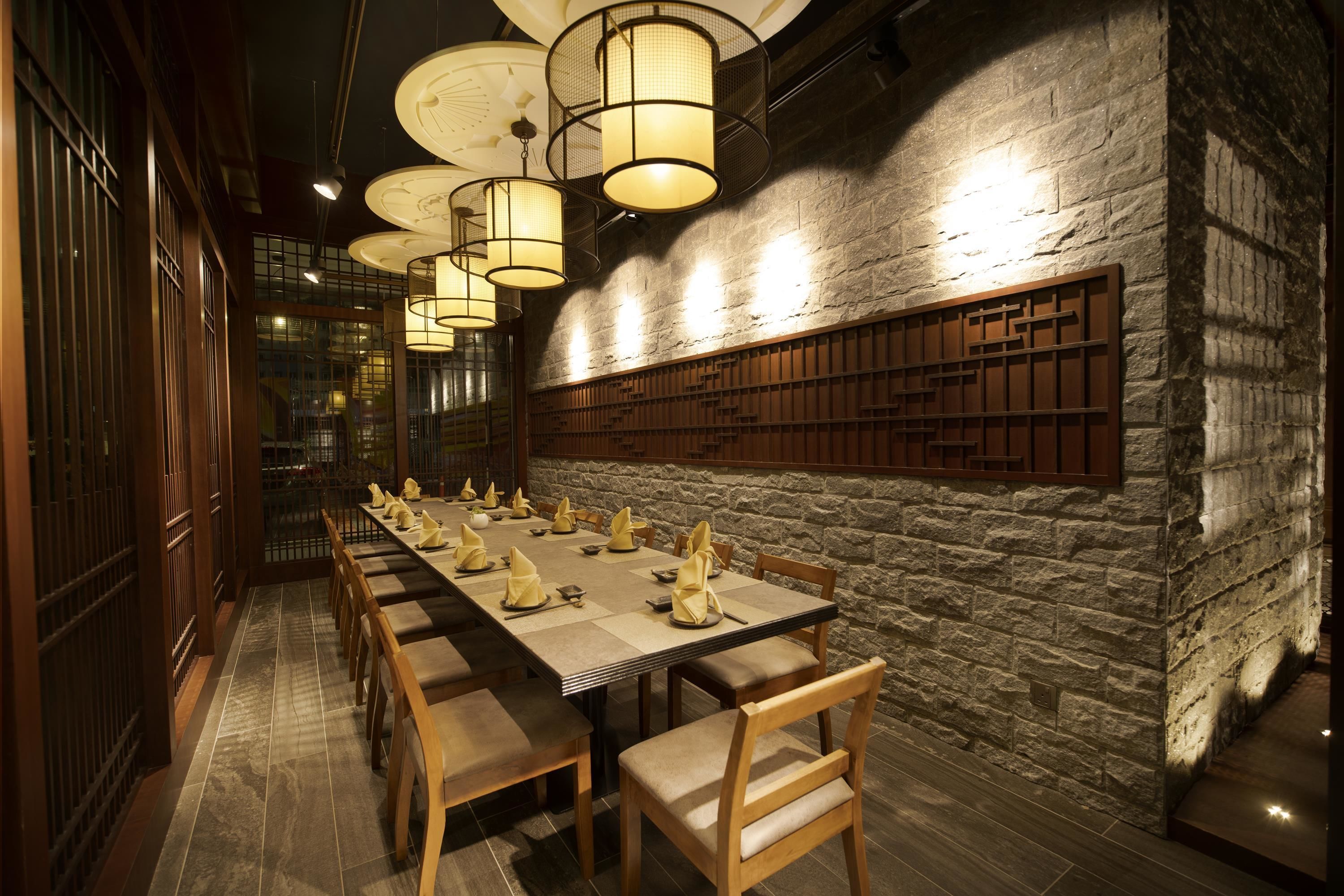 Una larga mesa de comedor dispuesta con sillas, paneles de madera y lámparas colgantes.