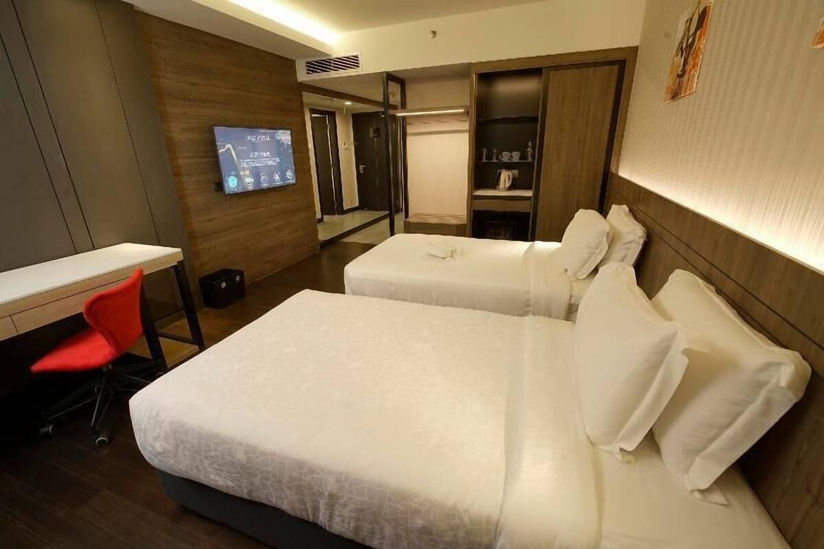 Ett hotellrum med två sängar, ett skrivbord, en röd stol, en tv och en garderob.