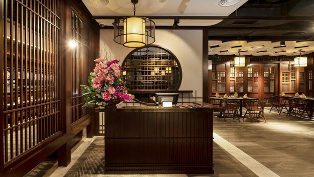 A reception area with a wooden reception desk, a large vase of pink flowers, and traditional Chinese-style wooden partitions. - Jazz Hotel Penang (George Town)
