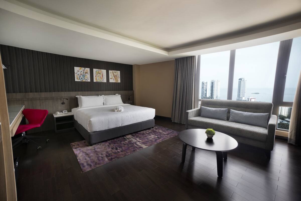 Ett modernt hotellrum med en stor säng, en soffa, ett skrivbord och utsikt över staden.