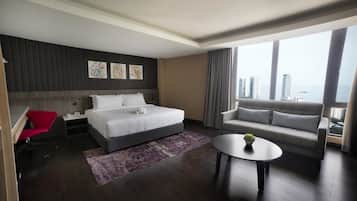Quarto de hotel moderno com uma cama grande, um sofá, uma mesinha e vista para a cidade.