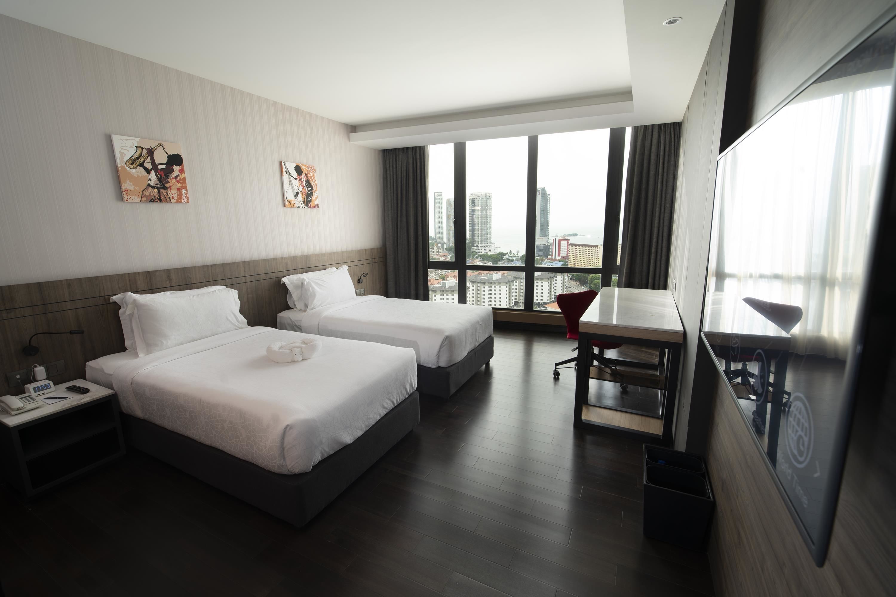 A hotel room with two beds, a desk, and a large window offering a city view.