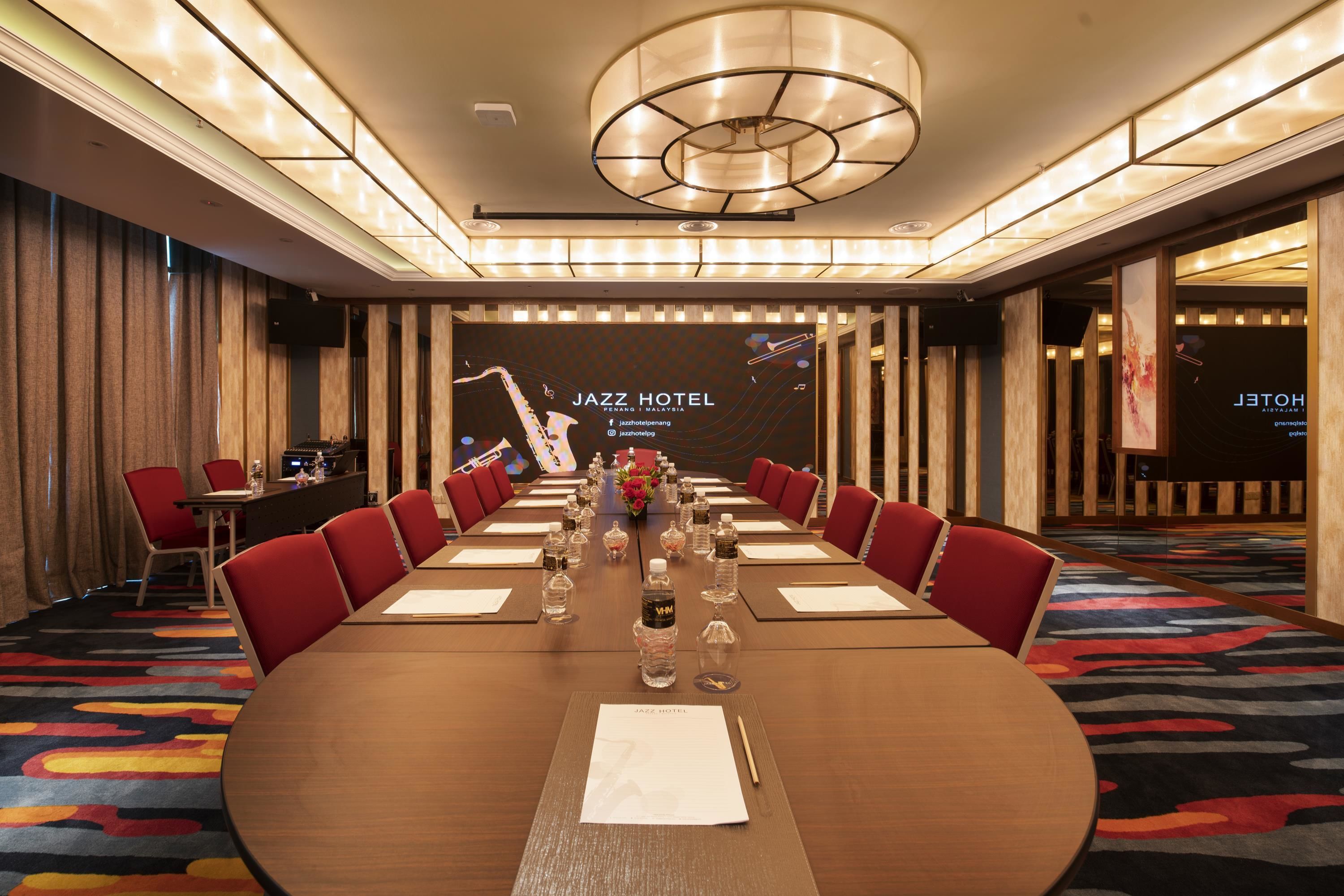 A conference room with a long table, red chairs, and a chandelier.