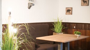 A corner seating area with a wooden table and a cushioned bench, surrounded by potted plants. - Hotel Garni - Dahlbrucher Hof (Hilchenbach)