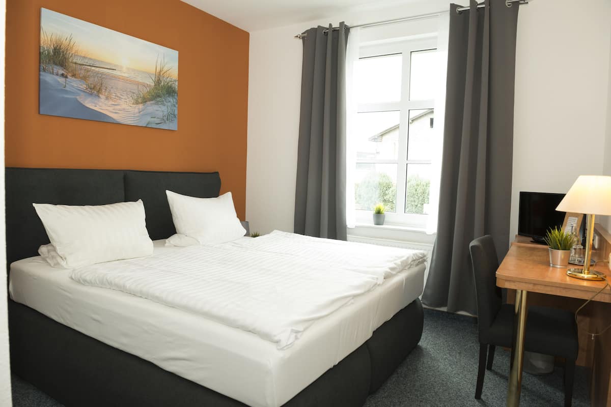 Quarto de hotel com cama, escrivaninha, cadeira, televisão e janela com cortinas.