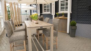 An outdoor patio with a wooden table and wicker chairs, surrounded by potted plants and umbrellas. - Hotel Garni - Dahlbrucher Hof (Hilchenbach)